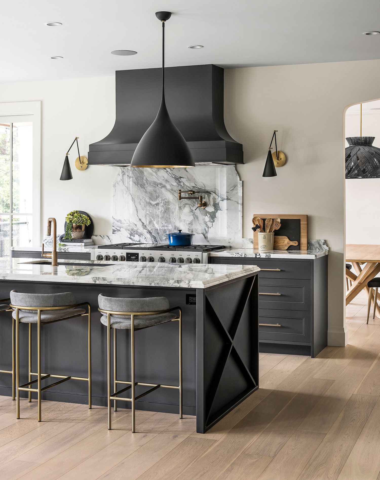 Elegant dark kitchen with black cabinetry, marble backsplash, gold accents, statement pendant lights, and a large island.