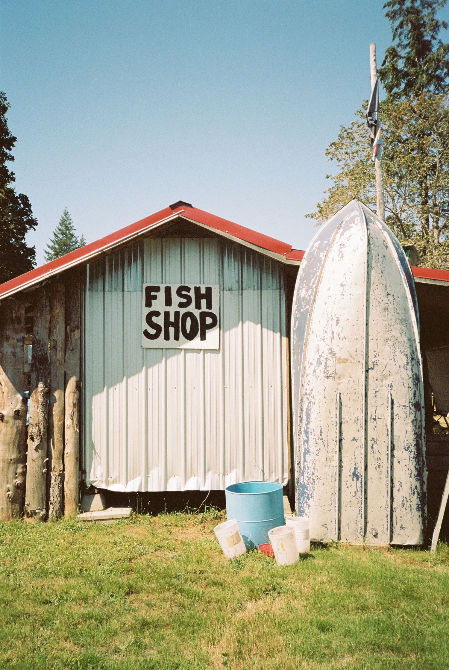 Rustic fish shop building with red roof, weathered boat hull leaning against wall, and blue bucket.