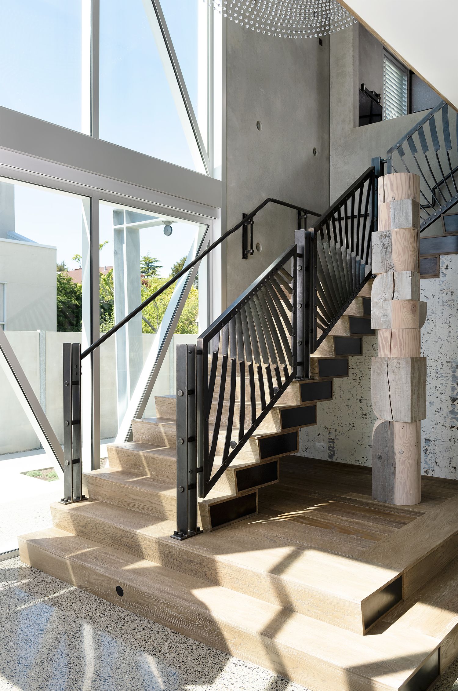 Modern interior staircase with black metal railing, light wood steps, and concrete walls in a contemporary home.