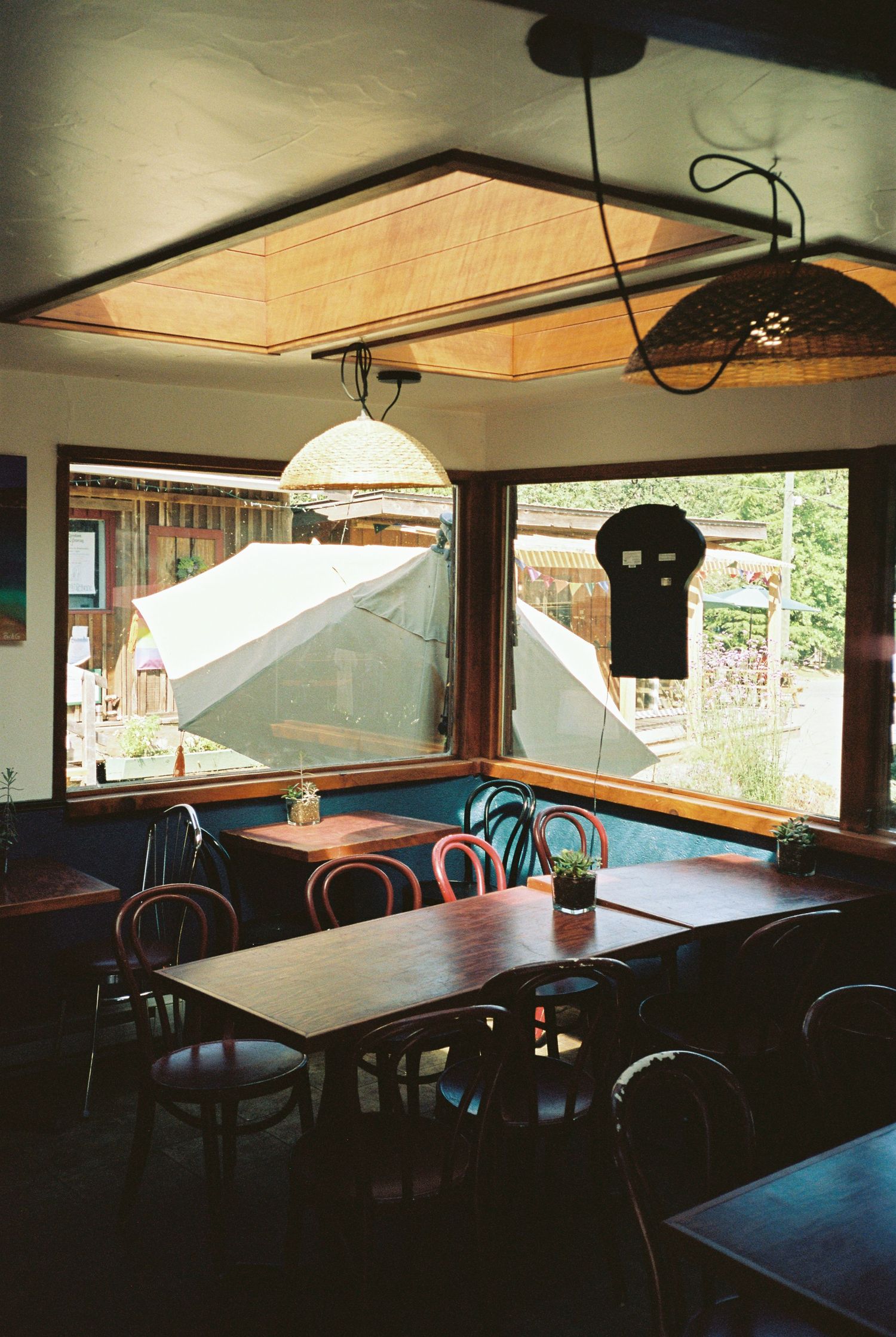 Cozy restaurant interior with wooden tables, bentwood chairs, pendant lights, and large windows.
