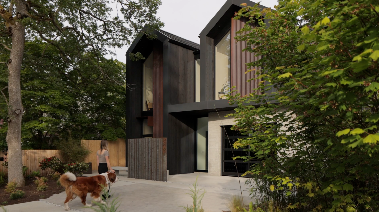 Modern dark wood two-story home surrounded by lush trees with a golden retriever in the foreground.