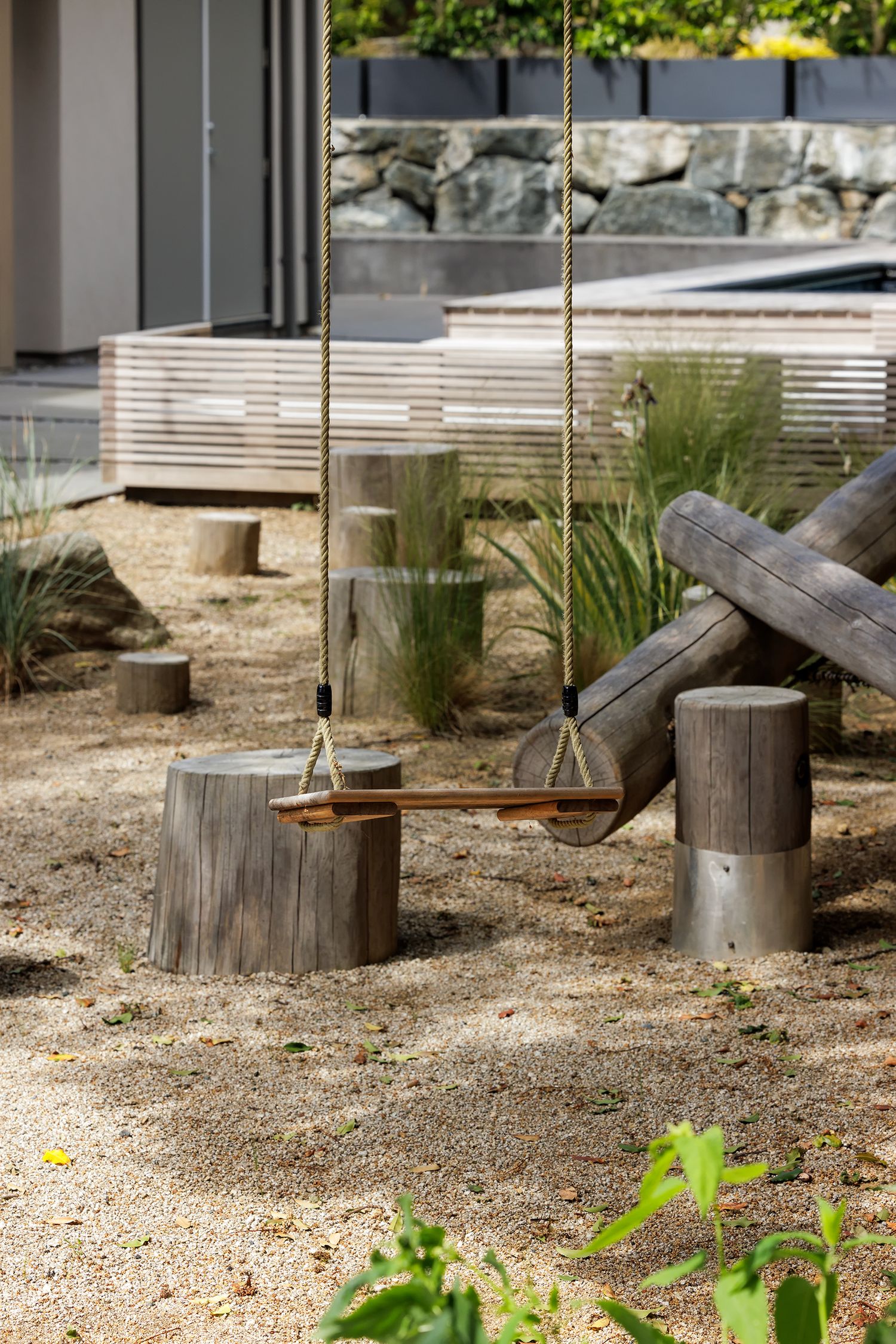 Rustic wooden swing with rope hangers surrounded by weathered tree stumps in a sandy natural playground area.