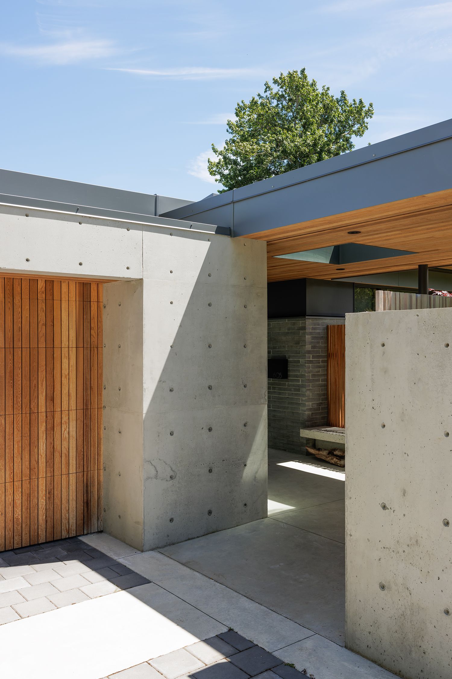 Modern concrete and wood home entrance with board-formed concrete walls and cedar door under blue sky.