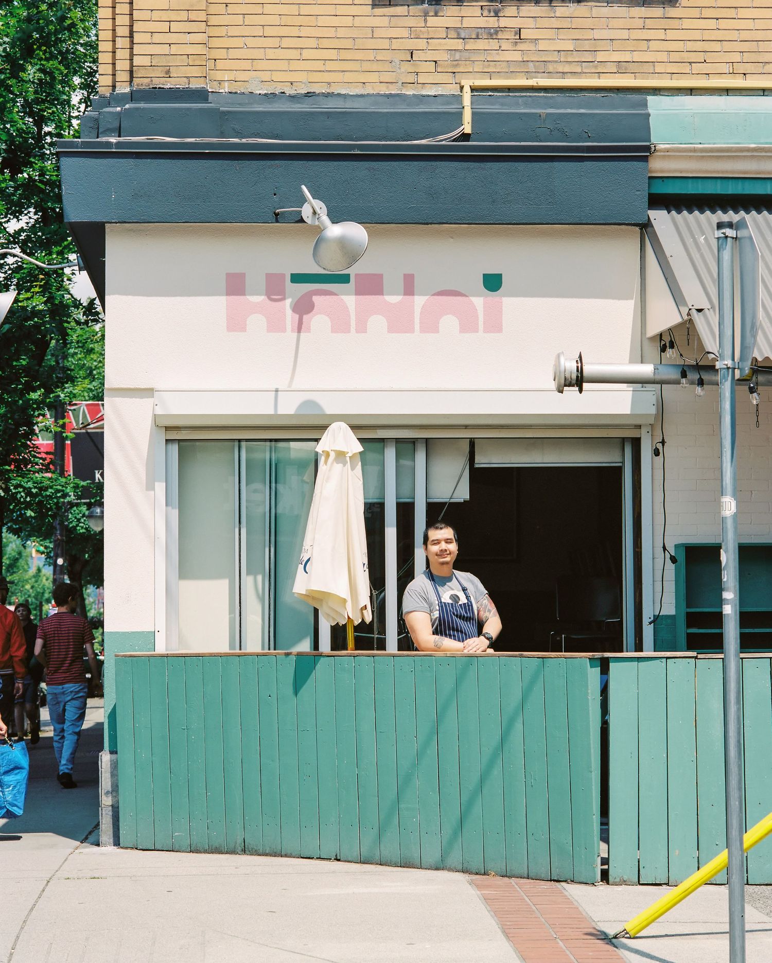 Man in apron stands at window of Hanoi restaurant storefront on urban street.