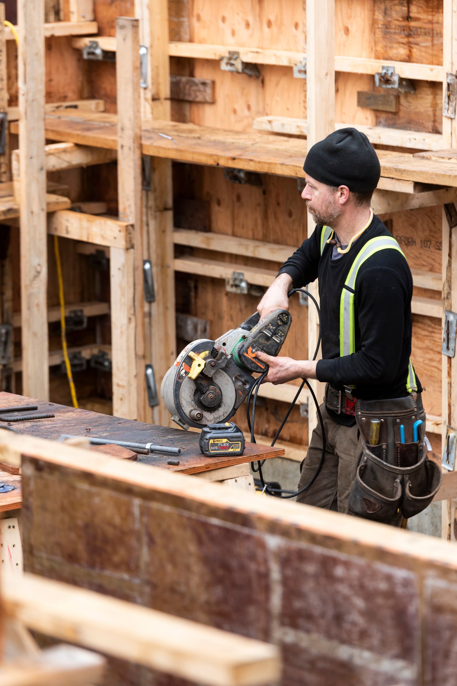 Construction worker in safety vest operating a circular saw on wooden formwork at an outdoor building site.
