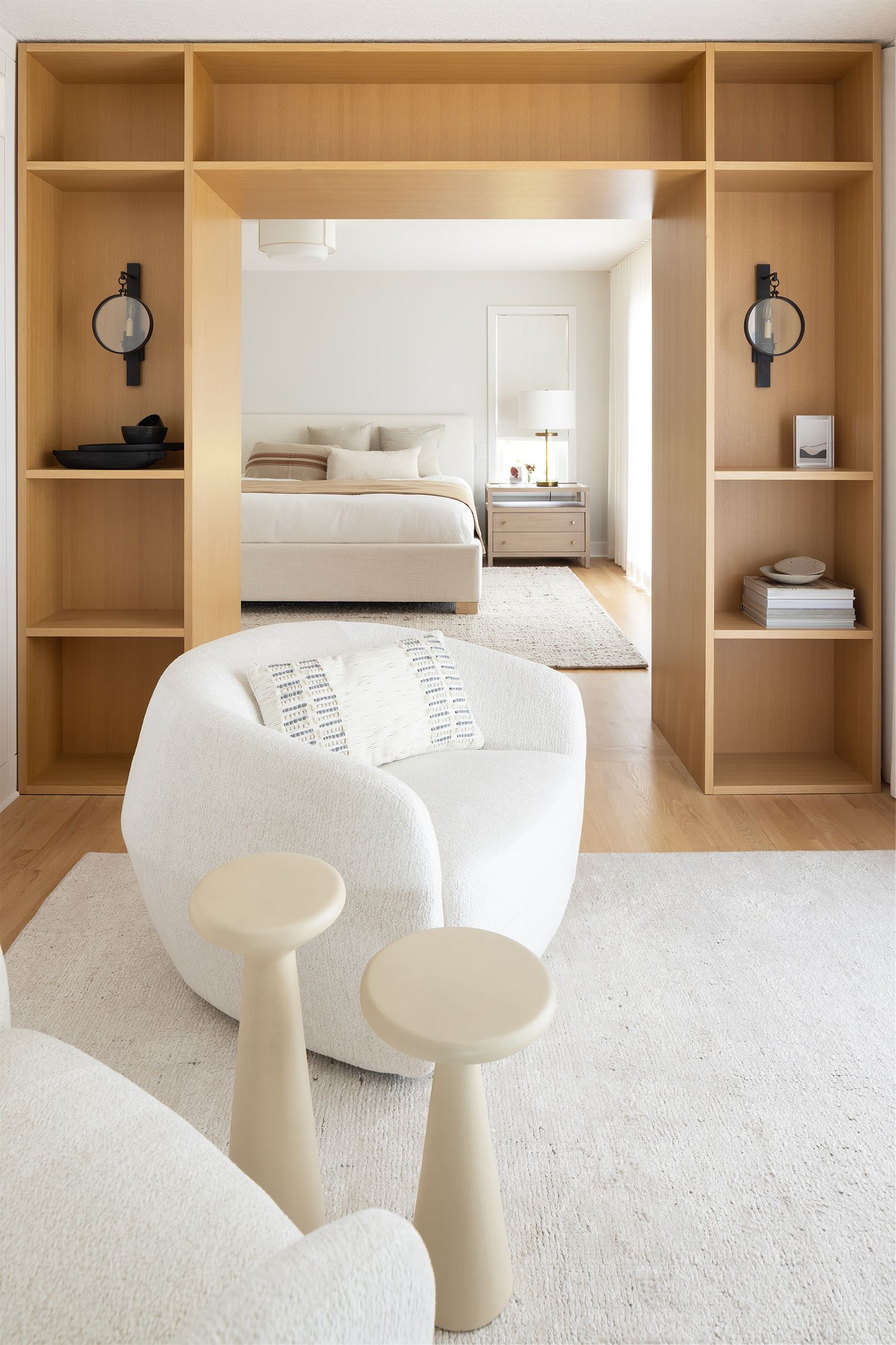 Elegant bedroom suite with built-in oak shelving unit framing doorway, white boucle chair, and neutral toned decor.
