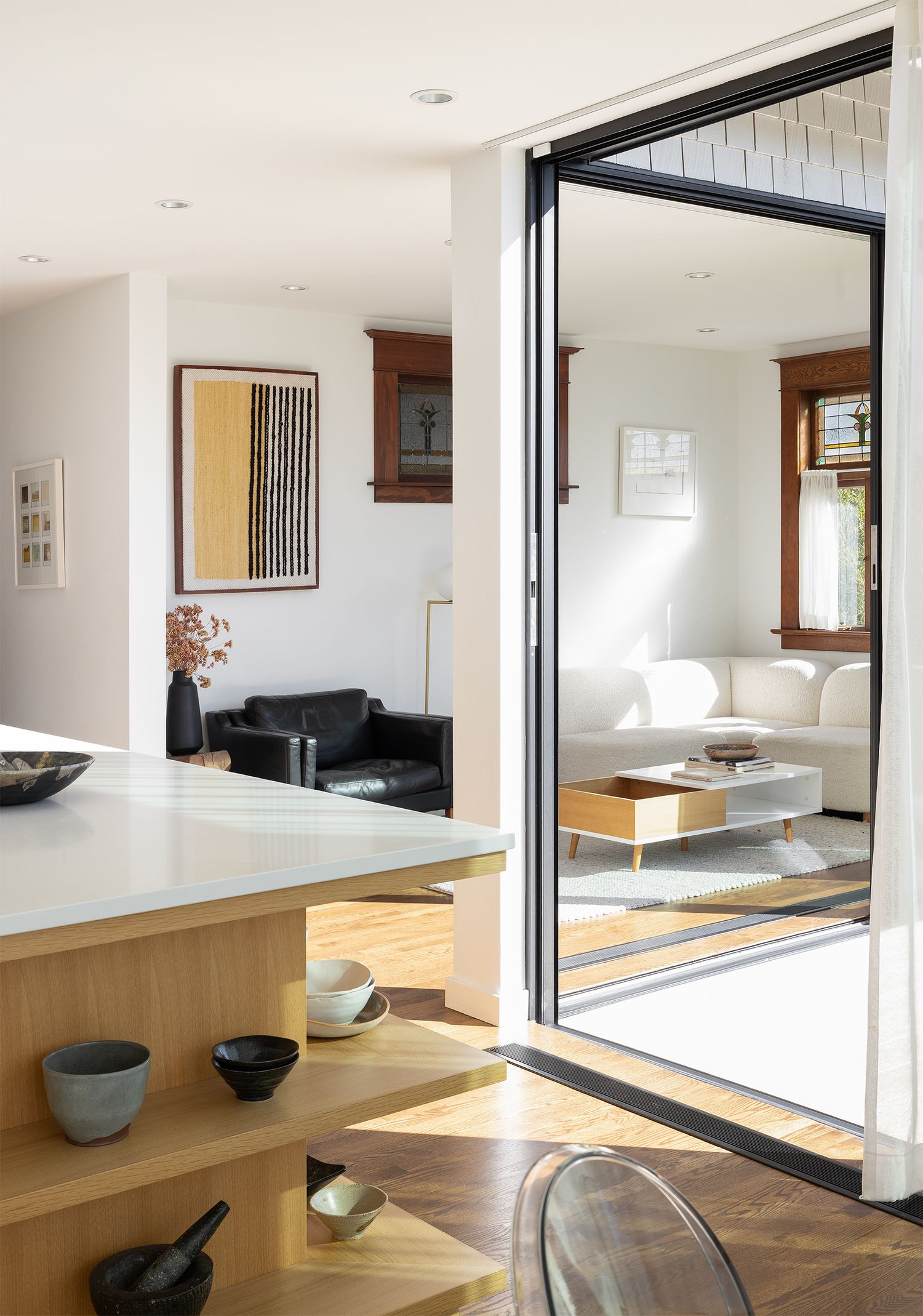 Contemporary open-plan interior with sliding glass door connecting kitchen to bright living room with modern art.