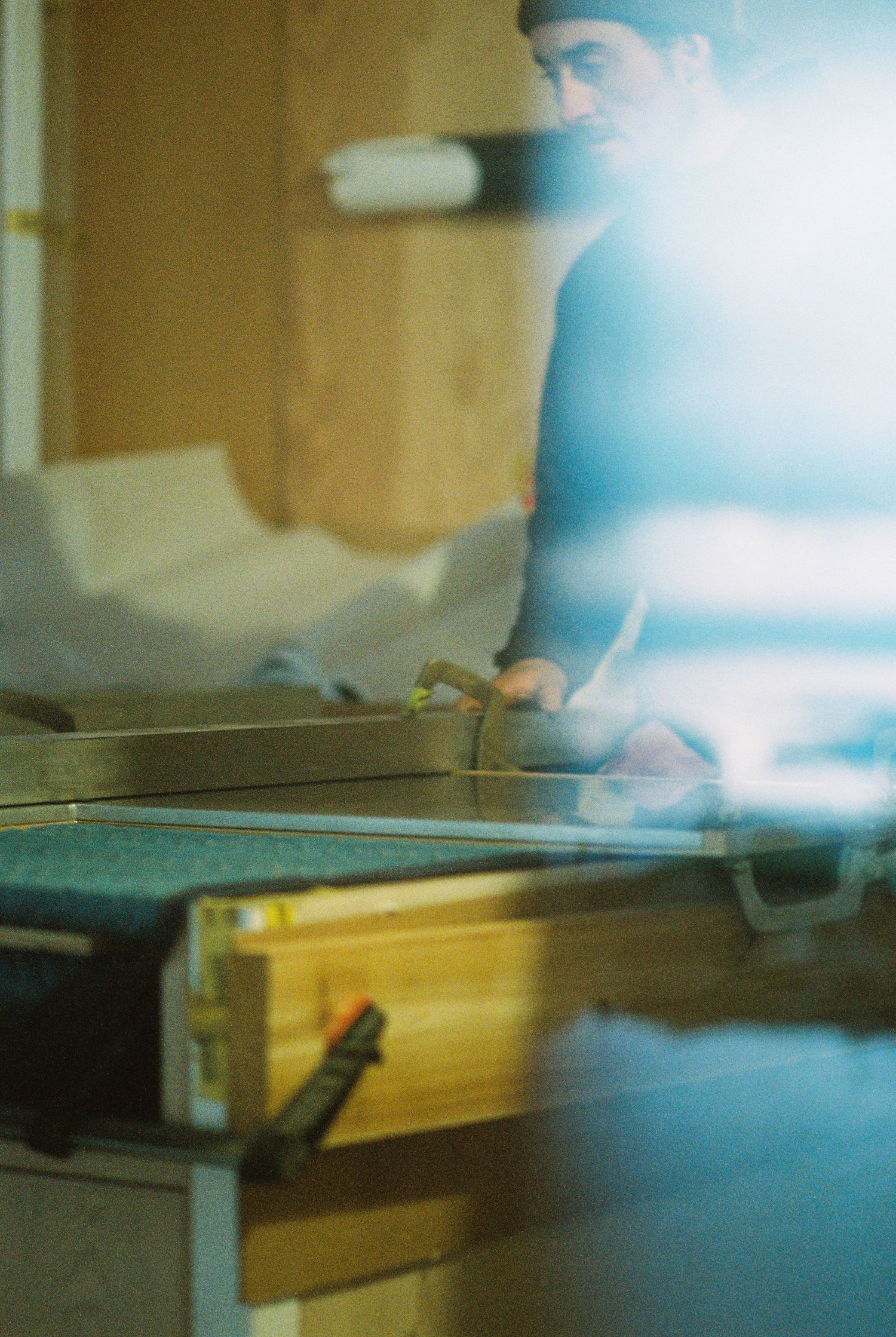 Film-exposed photo of a craftsman working at a table saw in a warmly lit woodworking workshop.