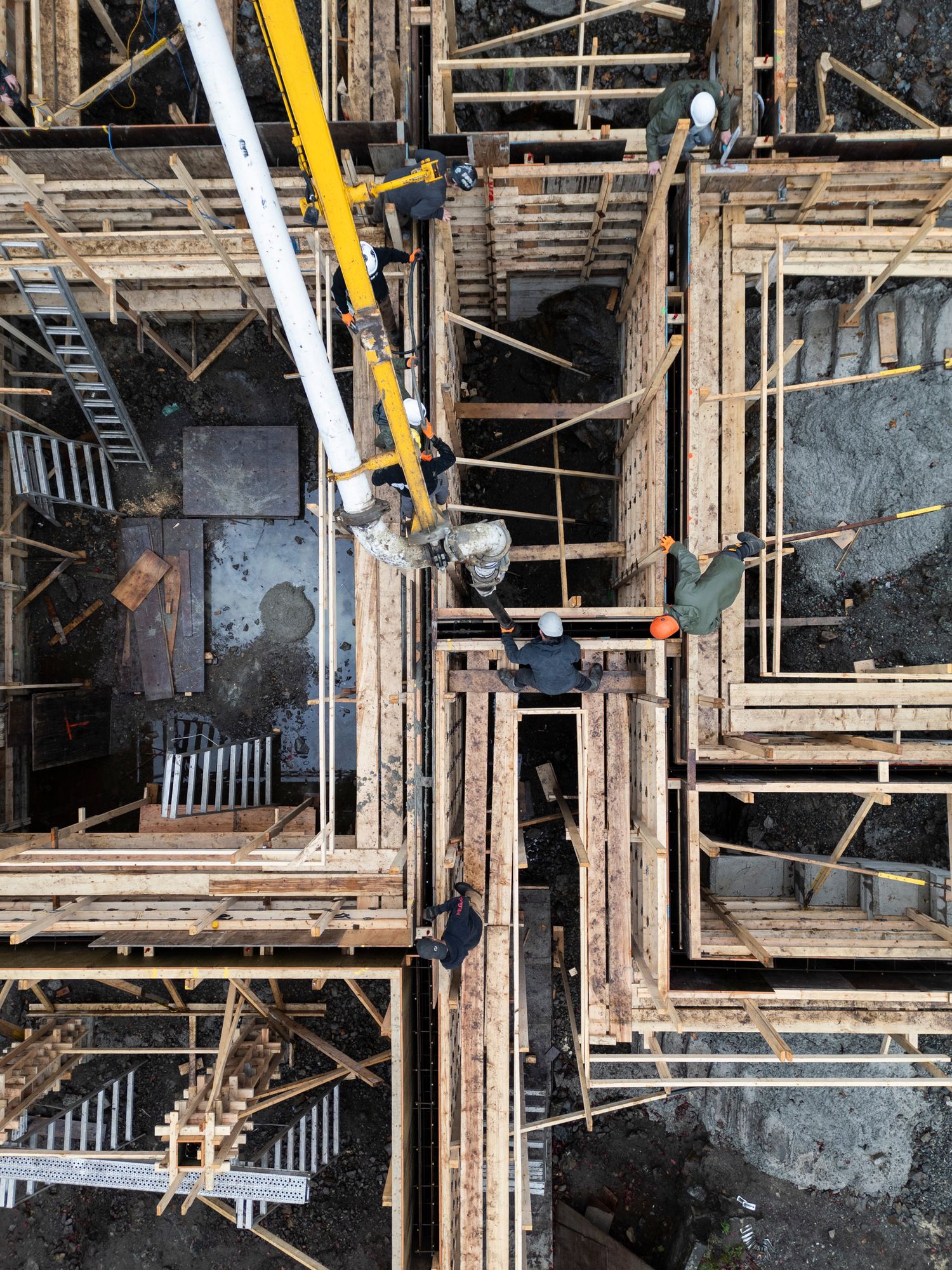 Aerial view of workers on wooden scaffolding framework at a construction site with crane equipment.