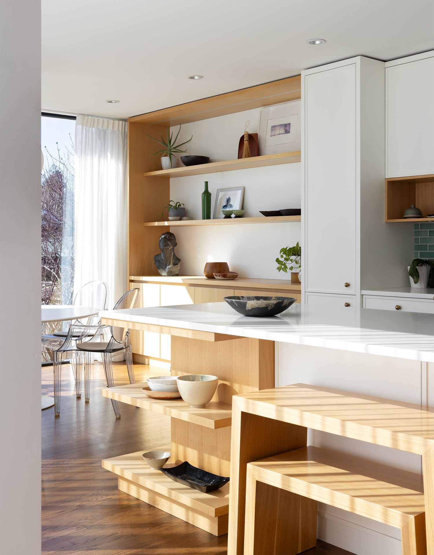Modern kitchen with natural wood shelving, white countertops, and minimalist wooden bench seating on herringbone floor.