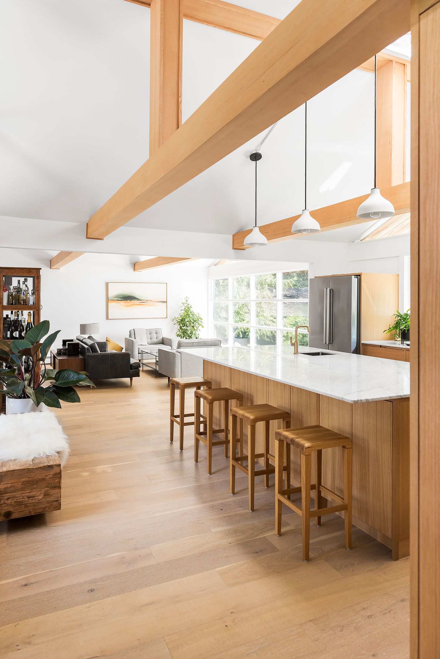 Open-concept kitchen and living room with vaulted wood beam ceiling, large island with bar stools, and hardwood floors.
