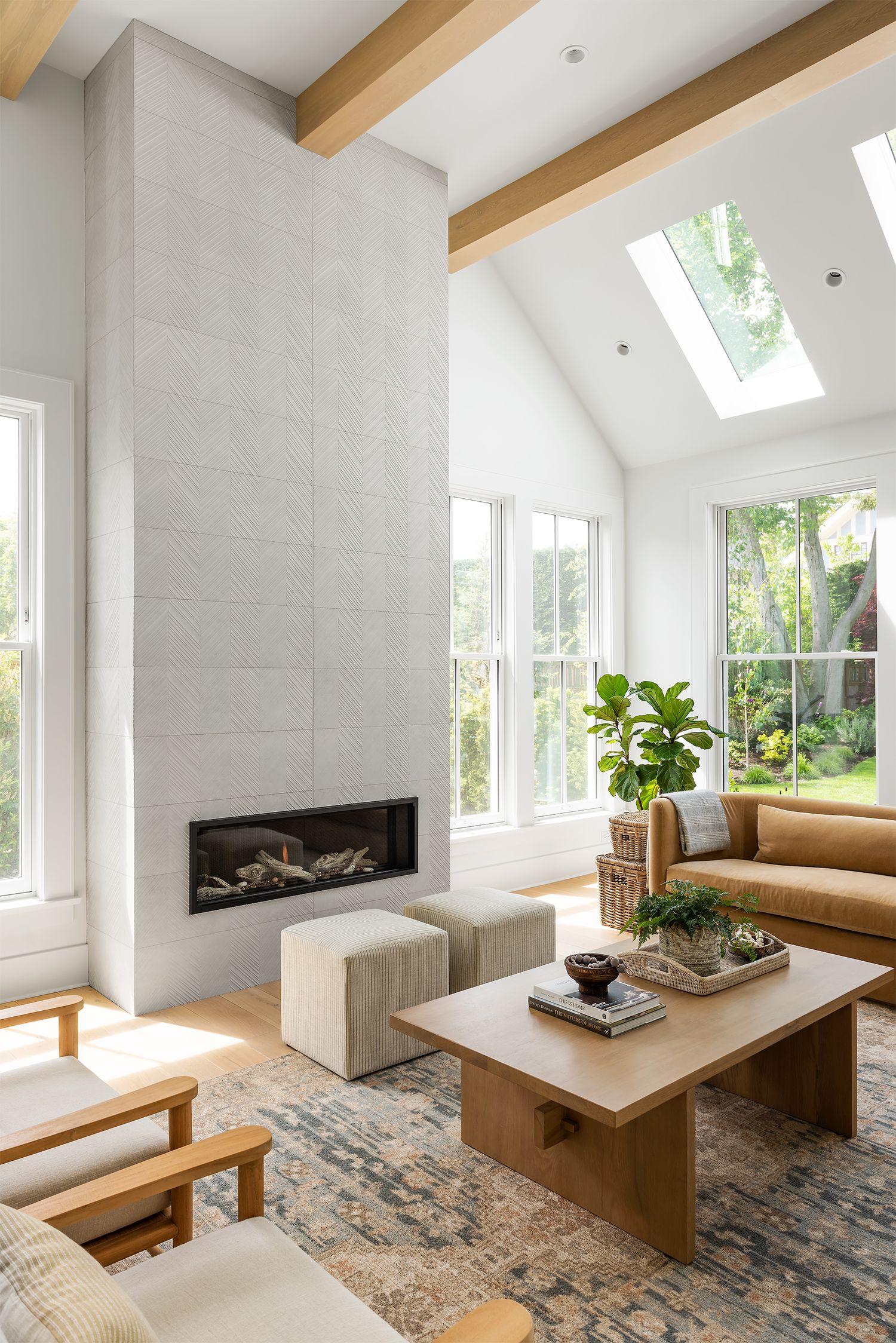 Bright modern living room with vaulted ceiling, skylight, floor-to-ceiling tiled fireplace, wood coffee table, and large windows.