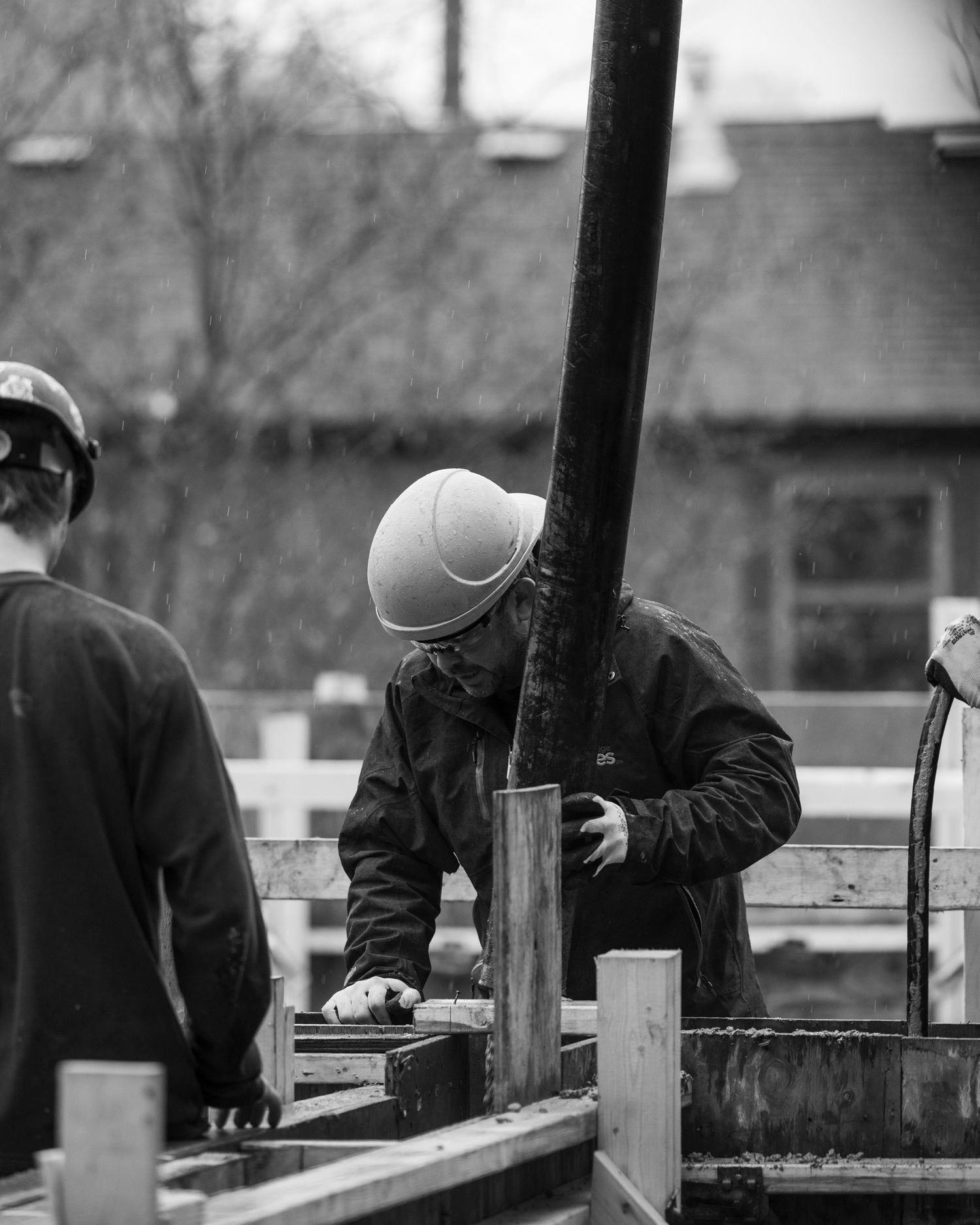 Black and white photo of construction workers in hard hats working with wooden forms at a job site.
