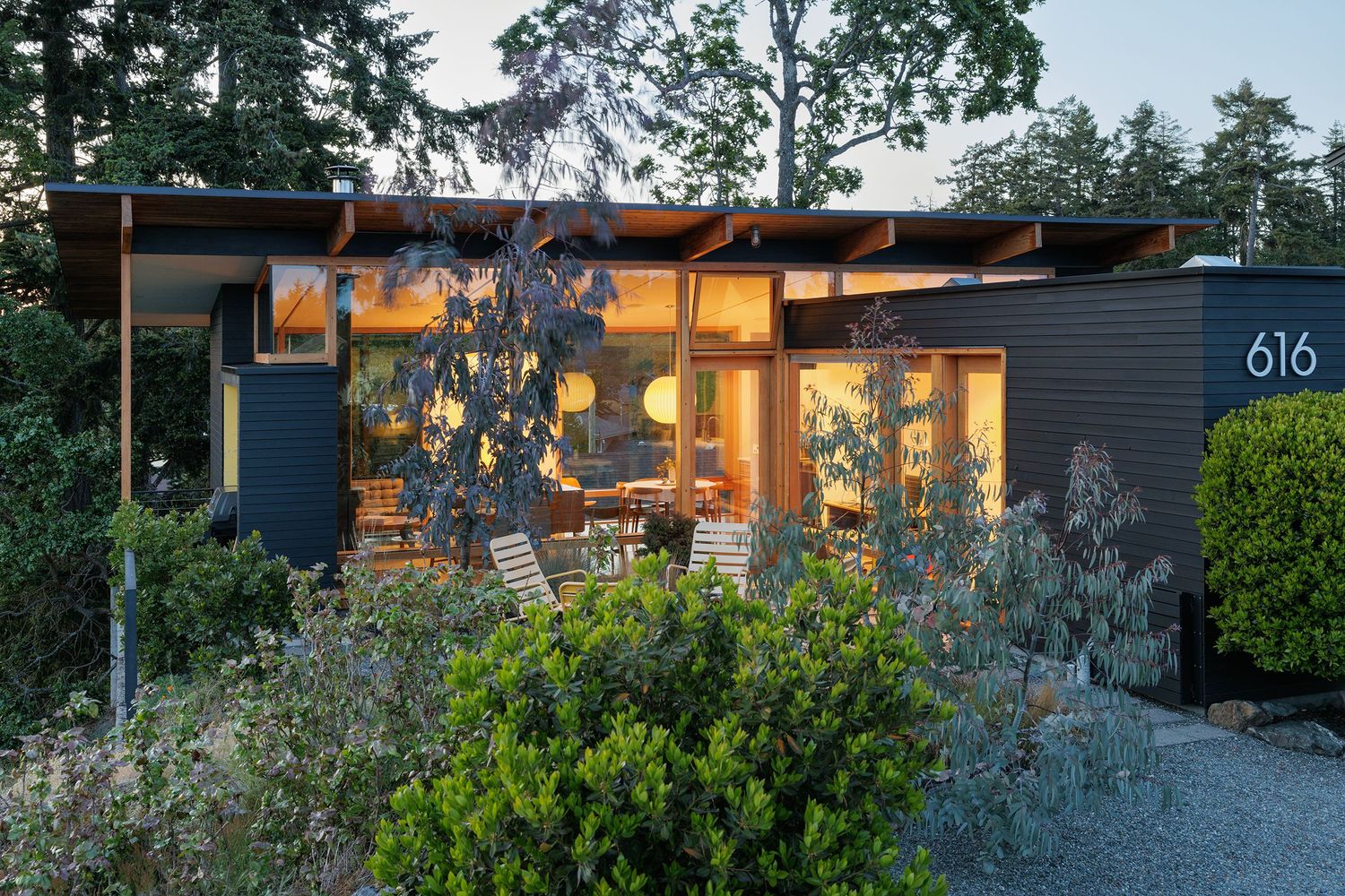 Mid-century modern home exterior at dusk with dark siding, large windows, globe lights, and address number 616.