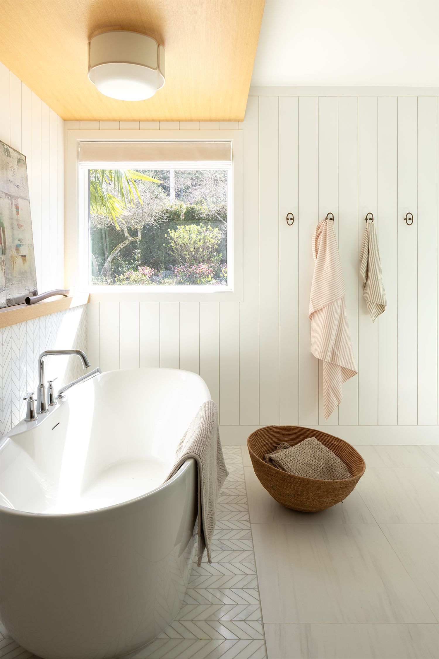 Bright minimalist bathroom with freestanding soaking tub, shiplap walls, herringbone tile floor, and garden window view.