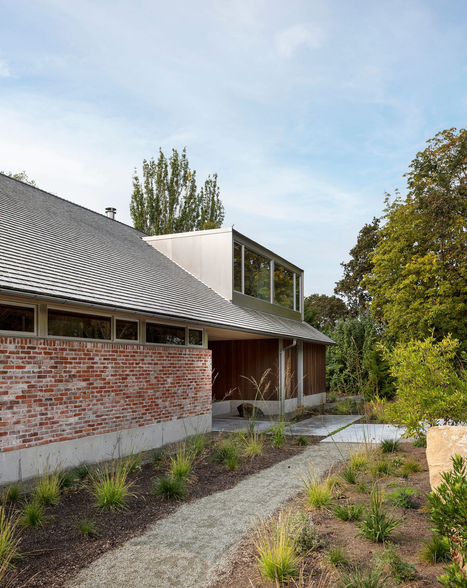 Brick and wood contemporary home with low-pitched metal roof surrounded by mature trees and landscaping.