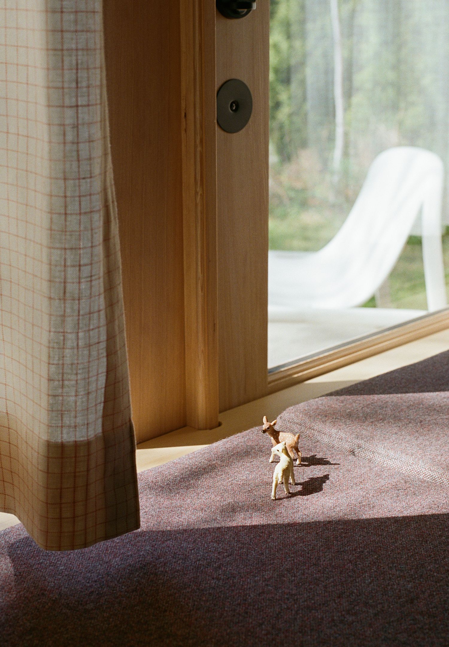 Small golden deer figurine on mauve carpet beside a wooden sliding glass door with sheer curtain.