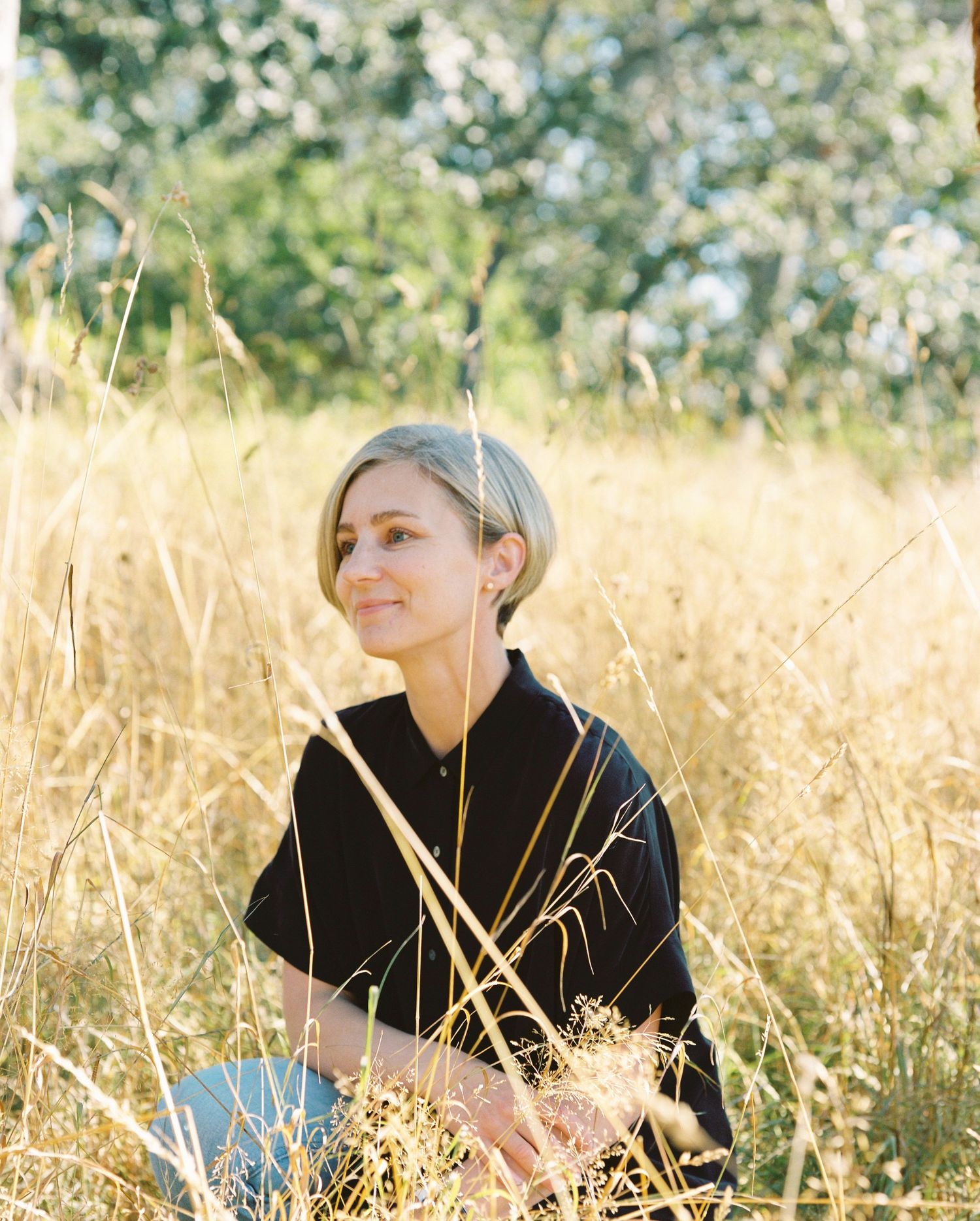 Young blonde woman sitting peacefully in golden tall grass field on sunny day.