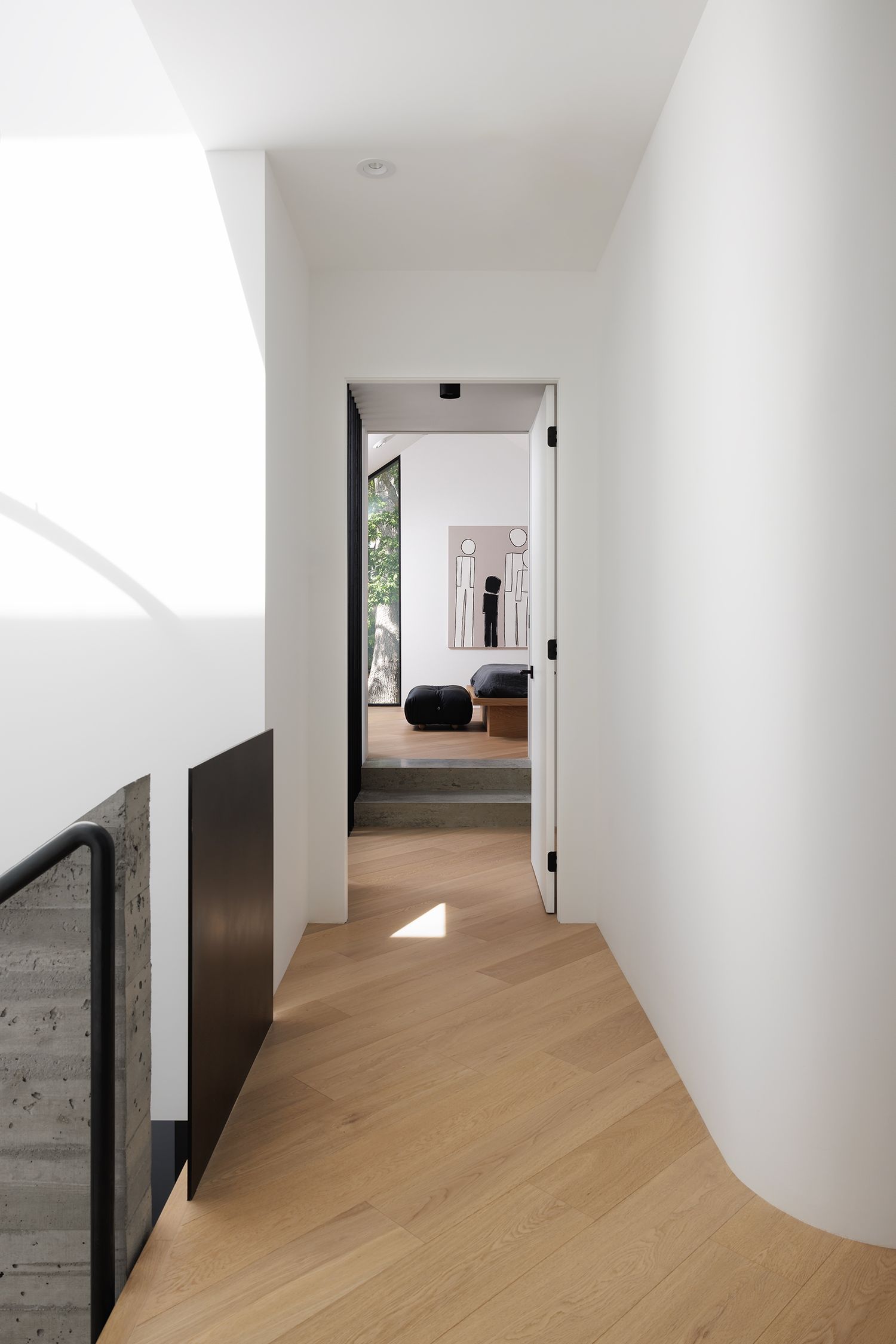 Minimalist white hallway with light oak herringbone floors, dark accents, leading to a serene bedroom with artwork.