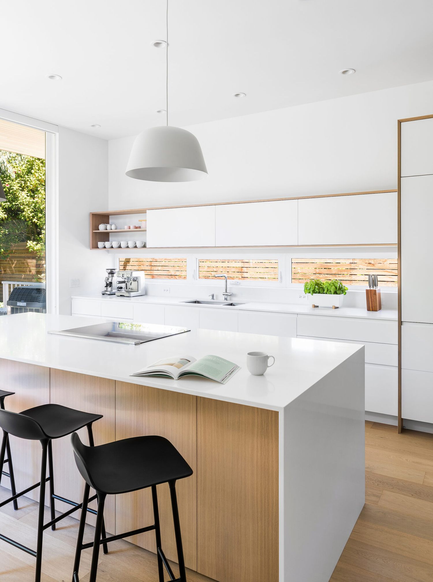 Sleek white and wood kitchen with island, black stools, dome pendant light, and open shelving backsplash.