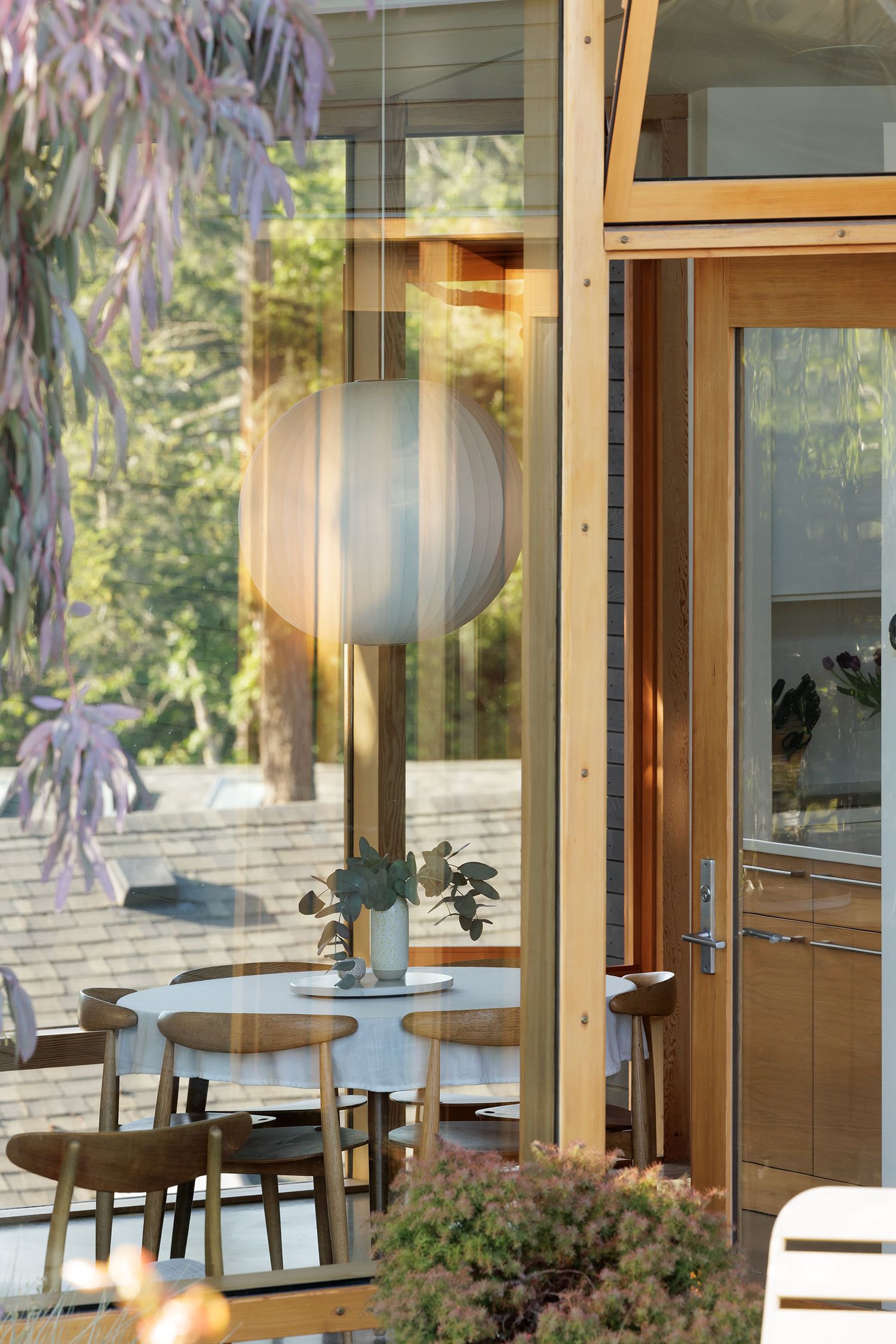 Mid-century modern dining area with round white table, wooden chairs, globe pendant light, and floor-to-ceiling windows.