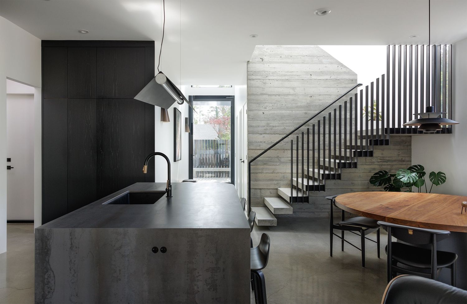 Sleek modern kitchen with dark stone island, black cabinetry, concrete staircase, and polished concrete floors in open layout.