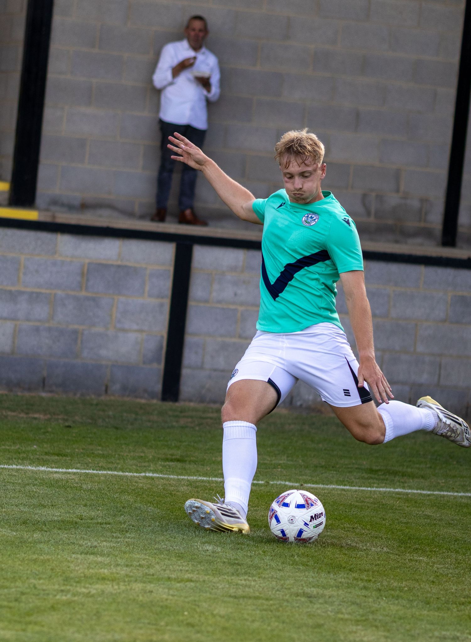A young footballer in a green and black kit prepares to strike the ball during a sunny outdoor match.