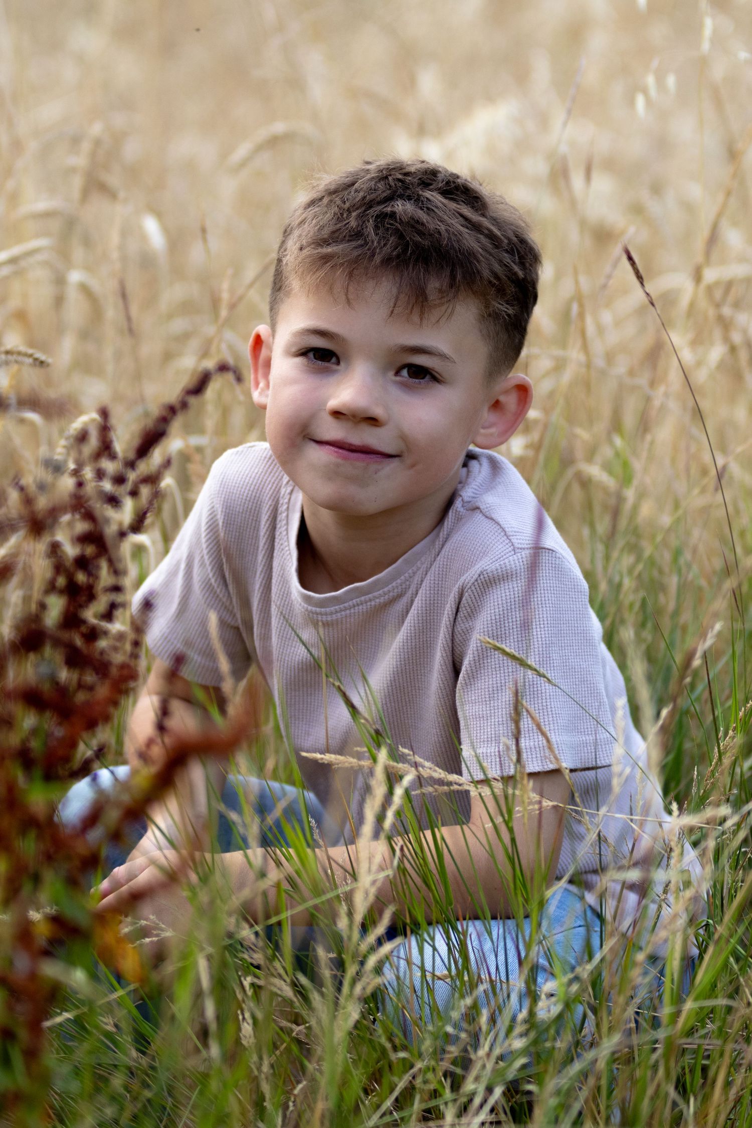 Young boy smiling while sitting in tall golden grass field during autumn.