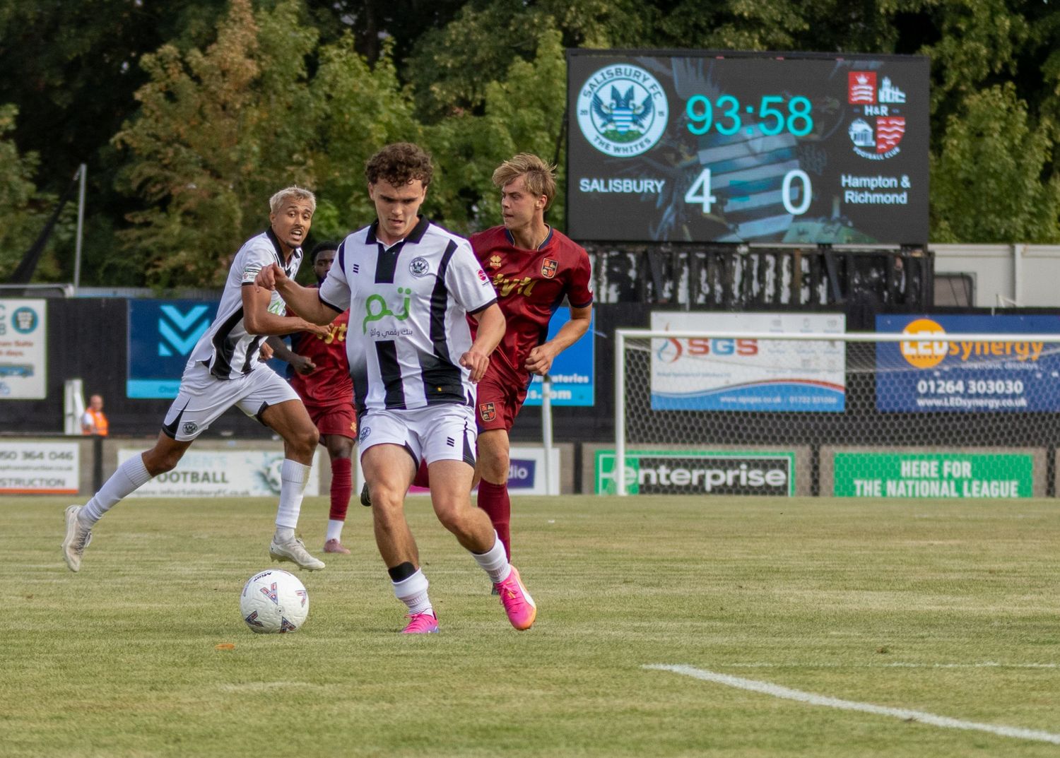 Salisbury FC player dribbles past opponent with scoreboard showing 4-0 win over Hampton Richmond.