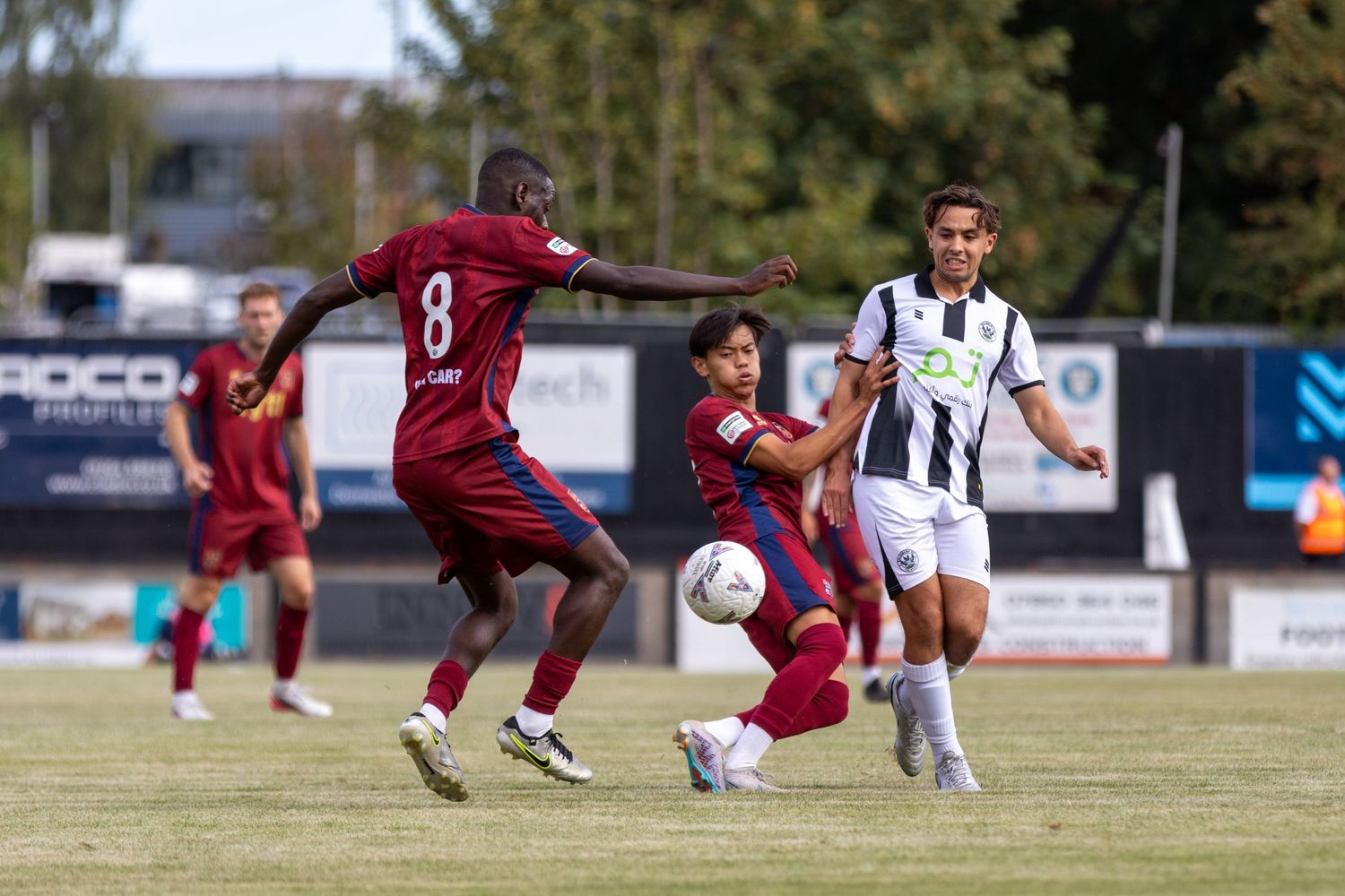 Player number 8 in maroon battles for possession against a black and white uniformed opponent on grass.