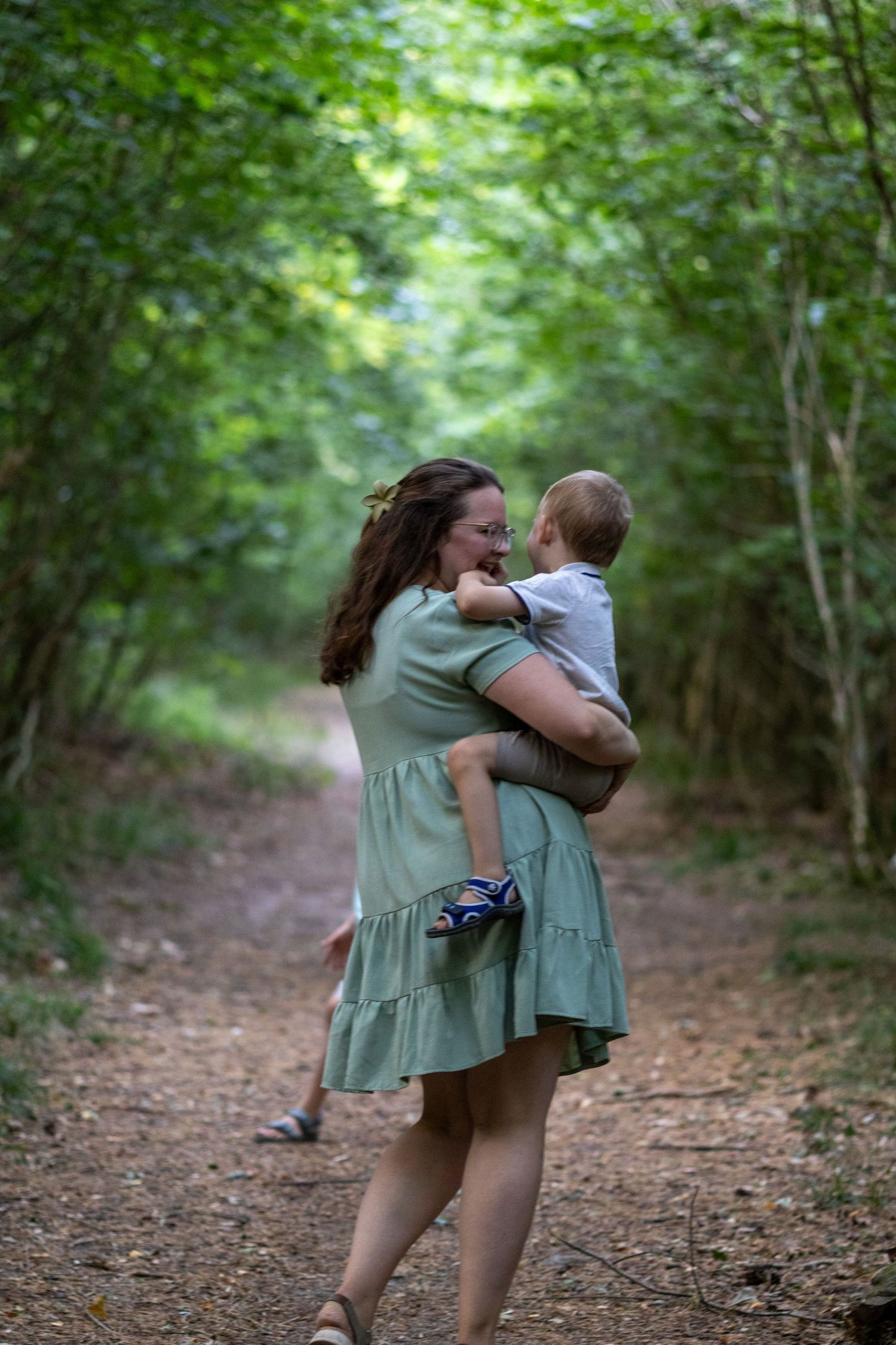 Loving mother nuzzling her baby boy on a tree-lined forest path.