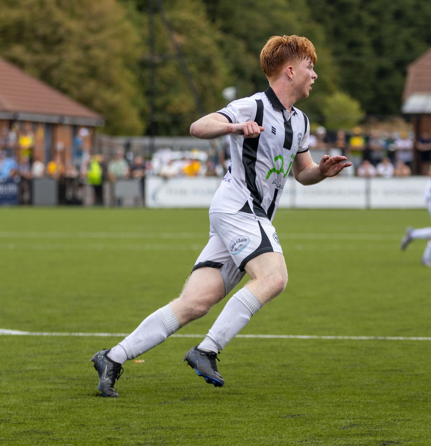 A red-haired footballer in black and white kit sprints across a grass pitch during a competitive match.