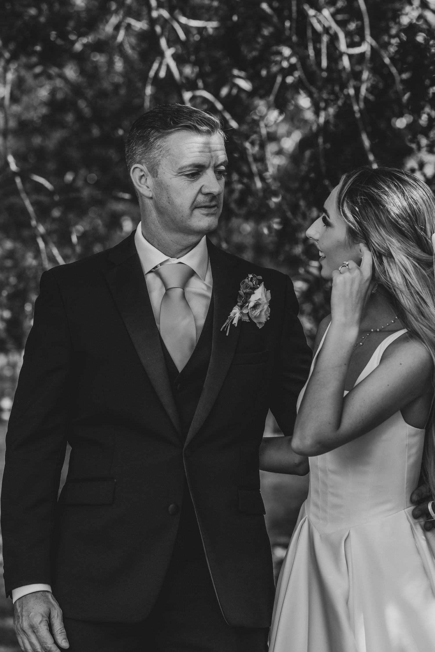 Black and white candid wedding photo of groom in tuxedo and bride in white dress sharing a moment.
