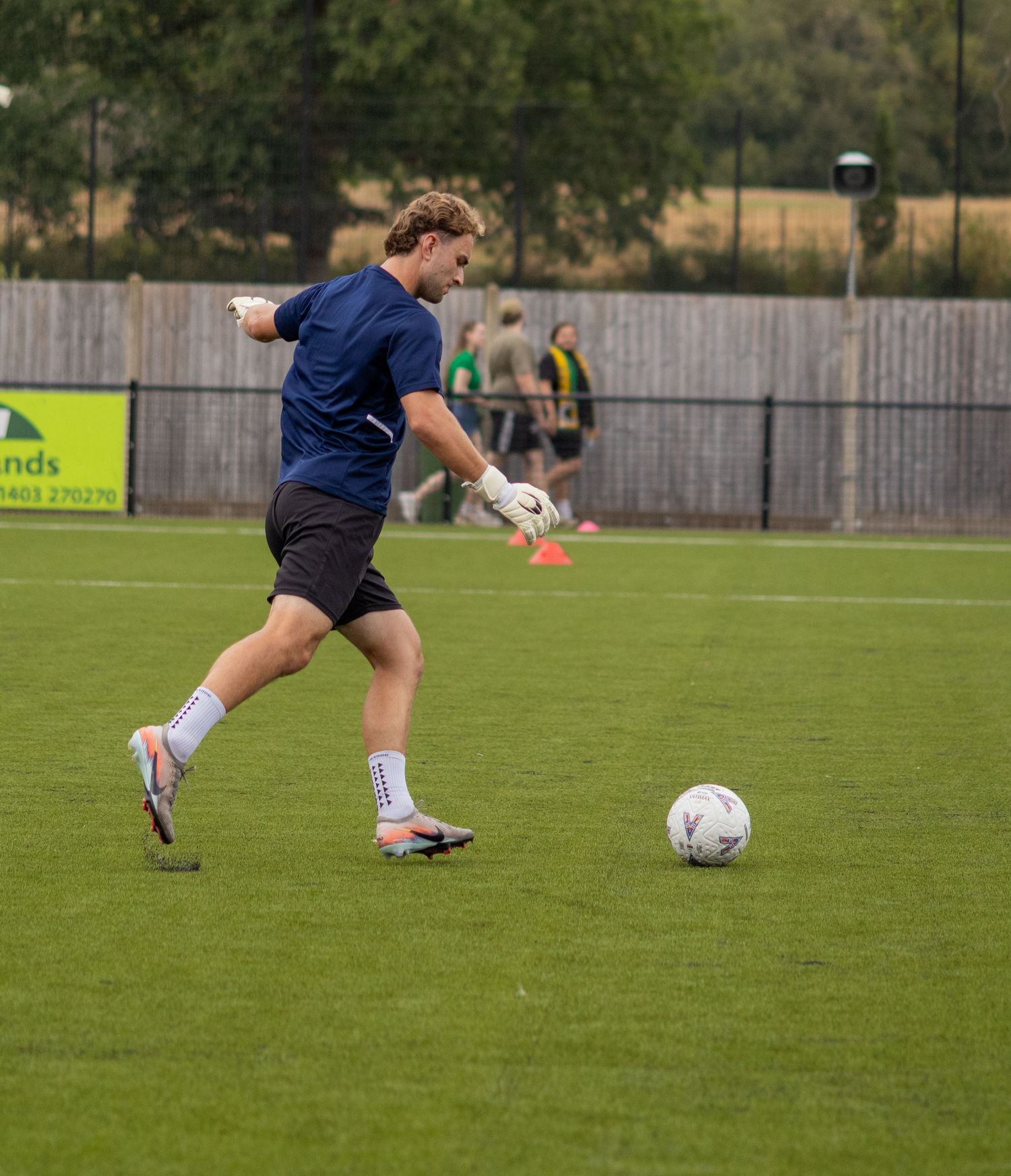 Young goalkeeper in blue training kit about to kick football on grass pitch.