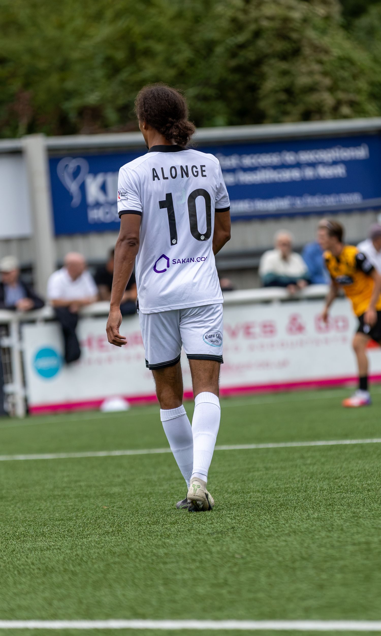Soccer player Alonge wearing number 10 white jersey walks on green pitch during a football match.