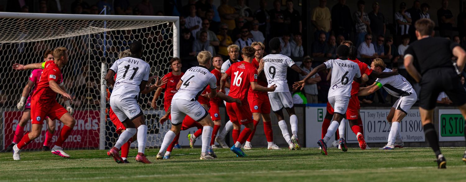 Soccer players compete in a crowded penalty box during an intense match, with red and white kits clashing near the goal.