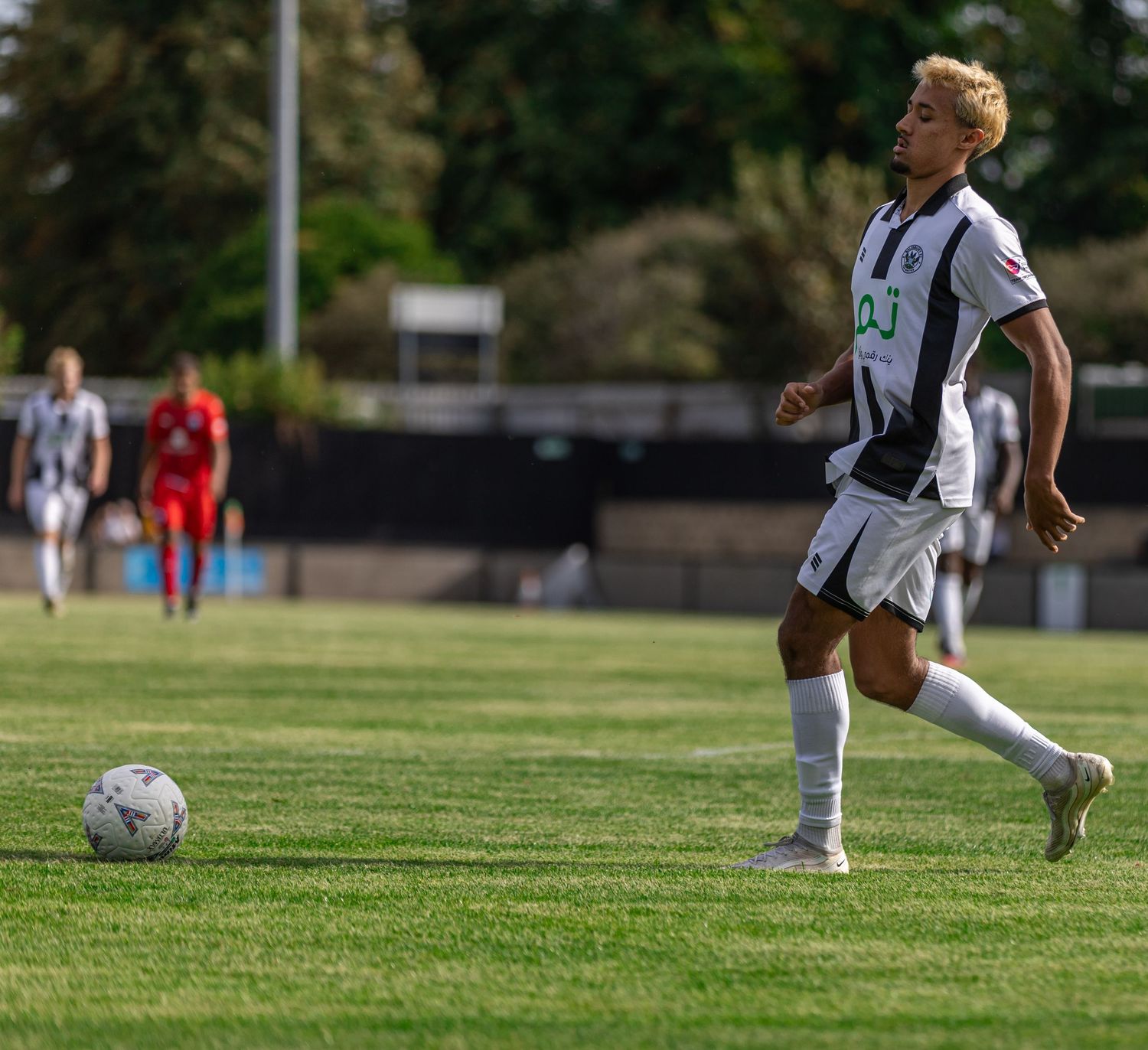 Young soccer player in black and white kit dribbling ball on green grass field during sunny outdoor match.