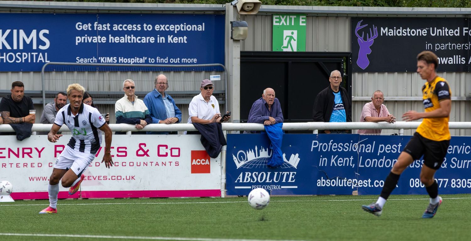 Two football players compete for the ball during a match at Maidstone United FC ground in Kent, England.