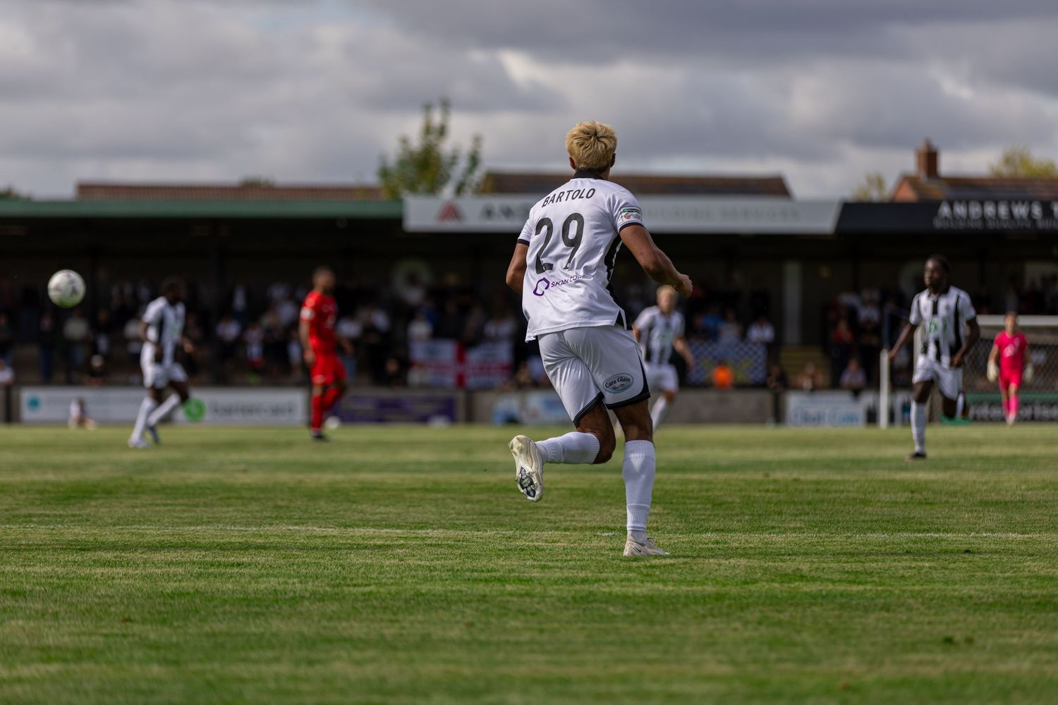 Soccer player number 29 in white kit sprints toward the ball during a sunny match at a grass stadium.