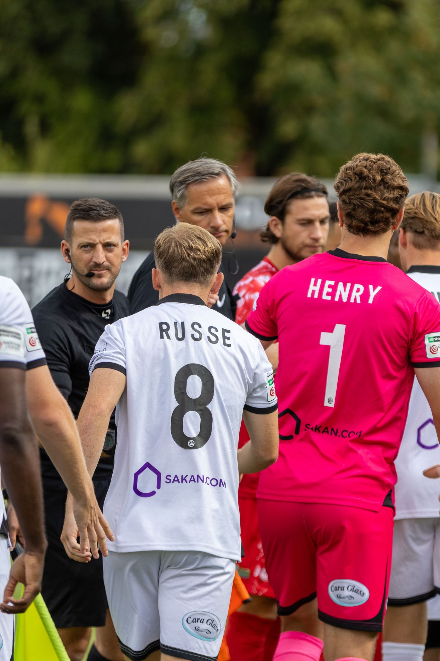 Football players including Russe number 8 and Henry number 1 meet referees pre-match.