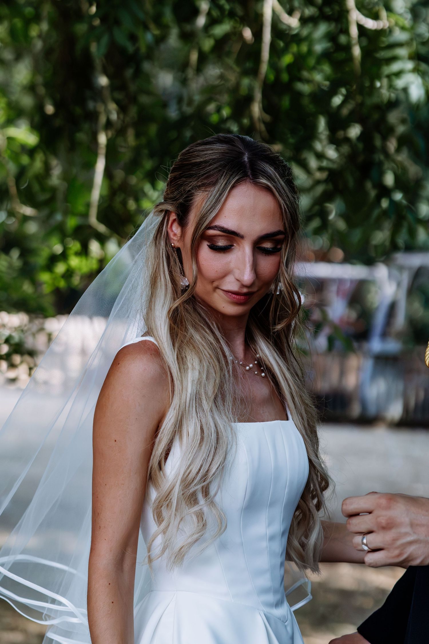 Beautiful bride in white gown with long blonde hair and veil looks down.