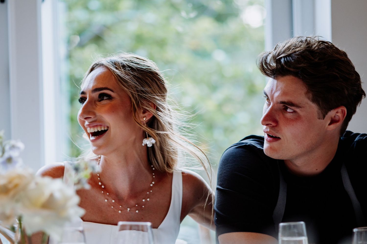 Happy bride and groom laughing together at elegant wedding reception dining table.
