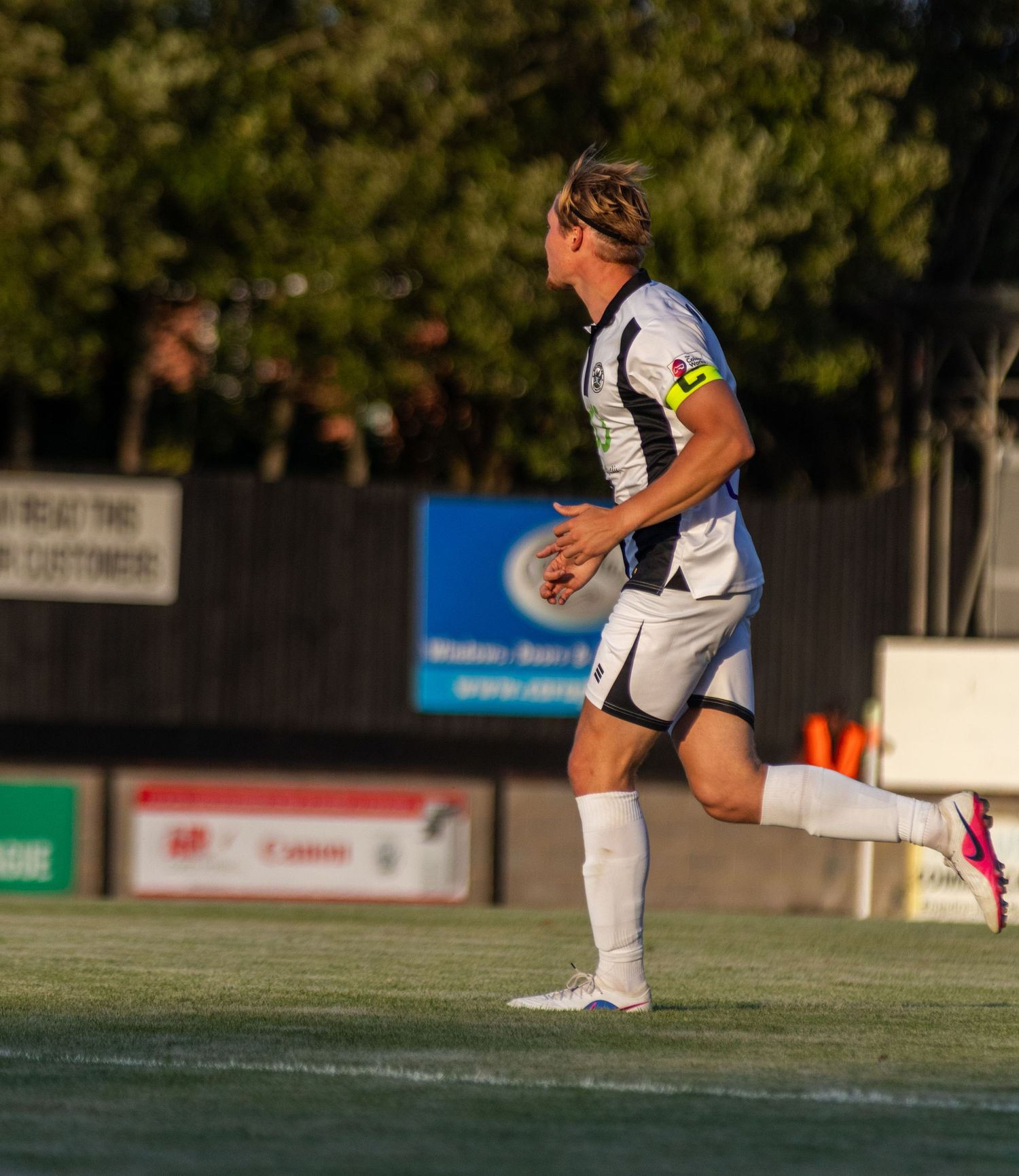 Soccer player in white and black kit running on grass pitch during evening match.