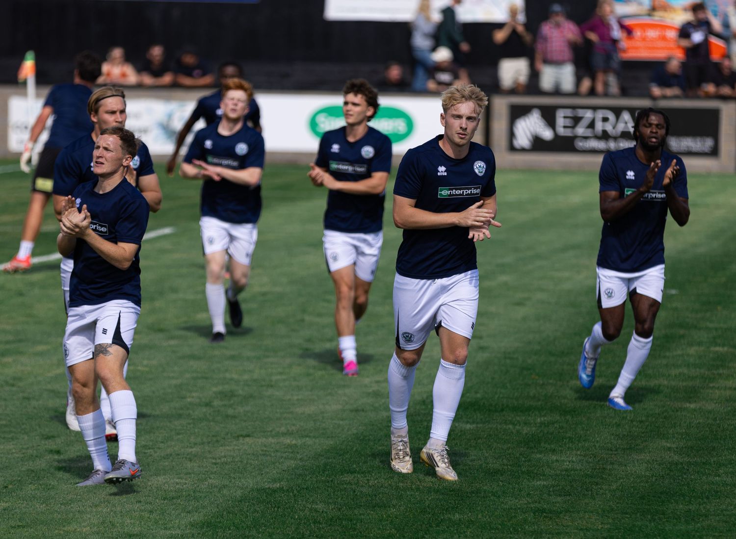 Soccer players in navy uniforms jogging on a green field during a warm-up before a match.