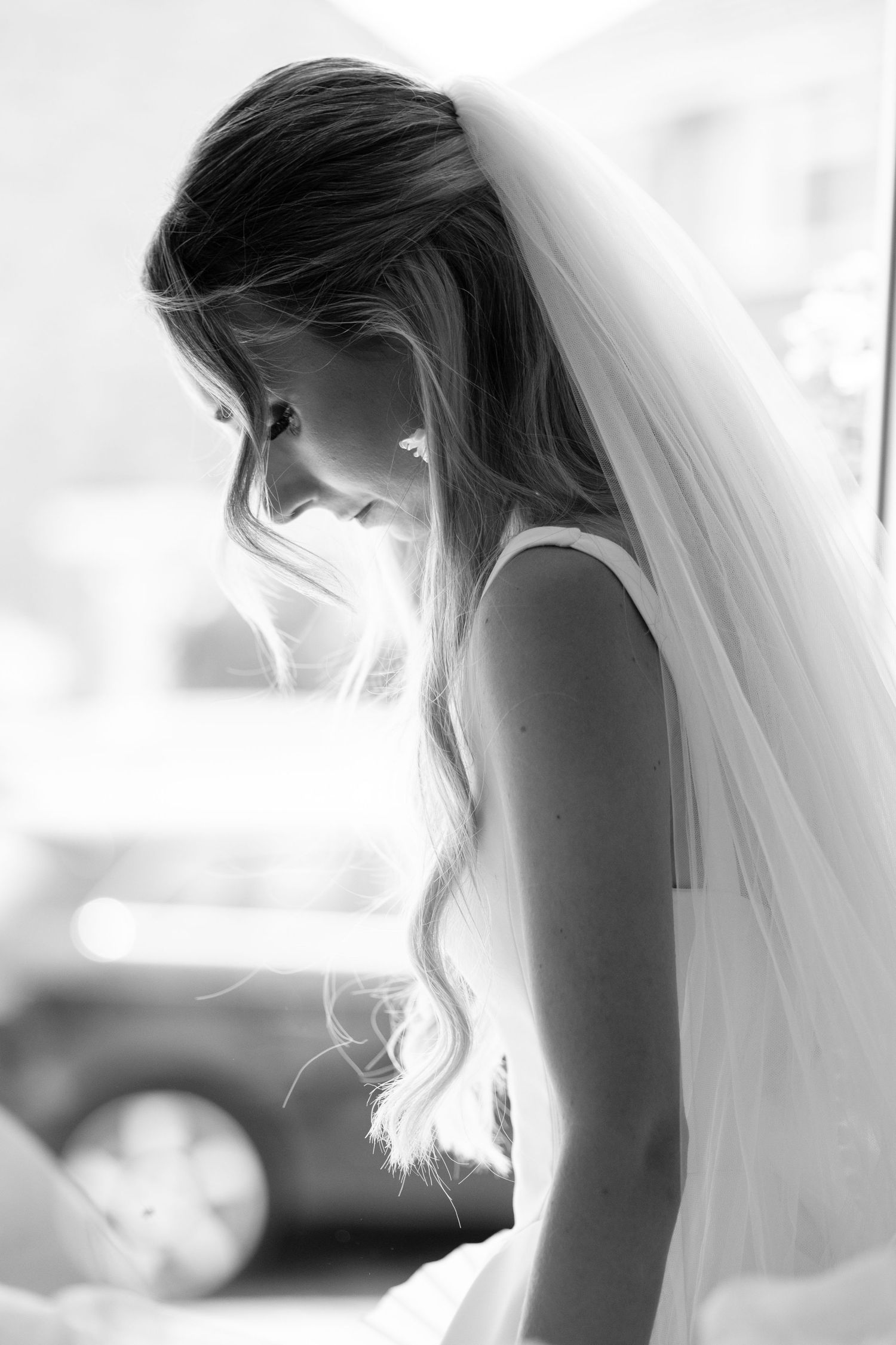 Black and white side profile of bride in white veil with long wavy hair looking down.