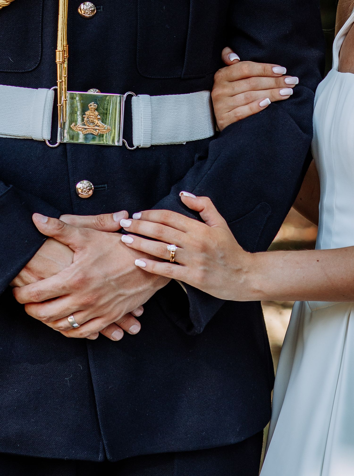 Close-up of bride and groom's hands showing wedding rings, groom in military dress uniform.