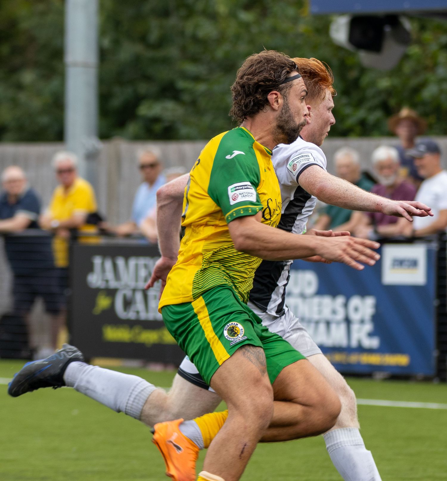 A yellow-green kitted footballer battles for position with a black-white opponent during an outdoor match.