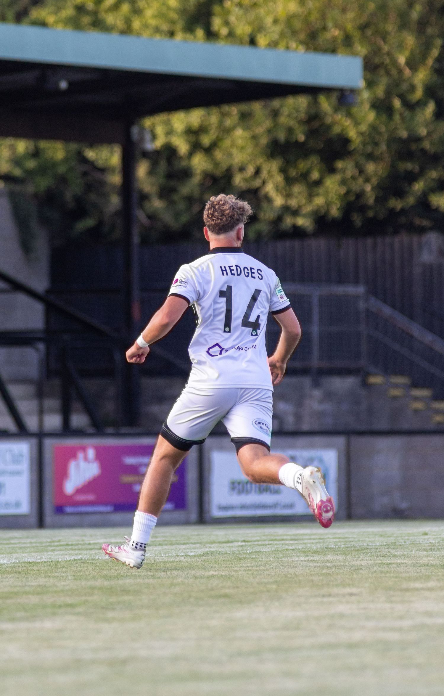 Footballer Hedges number 14 in white kit running away from camera on green pitch.