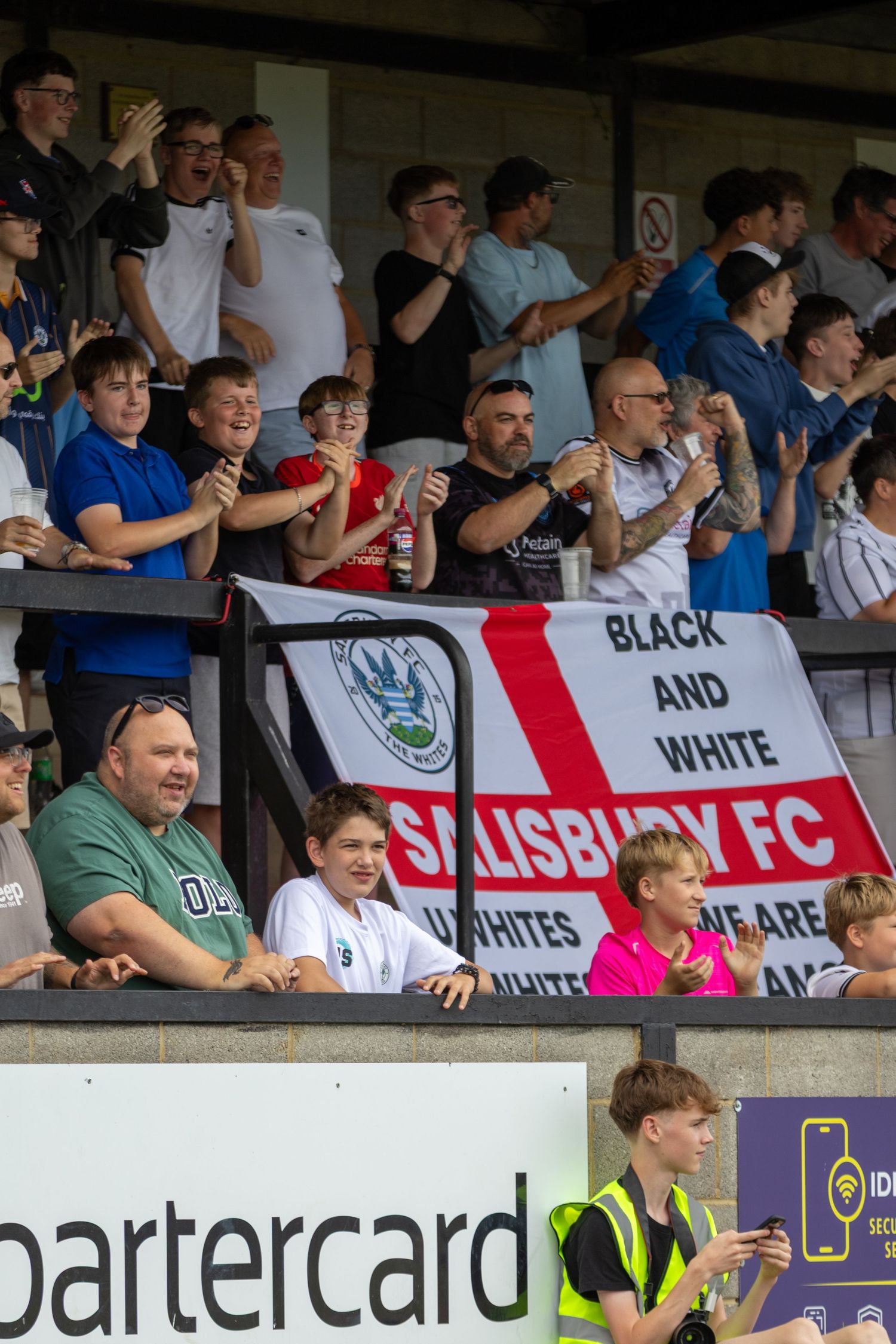 Enthusiastic Salisbury FC fans cheering in the stands with Black and White banner during a match.
