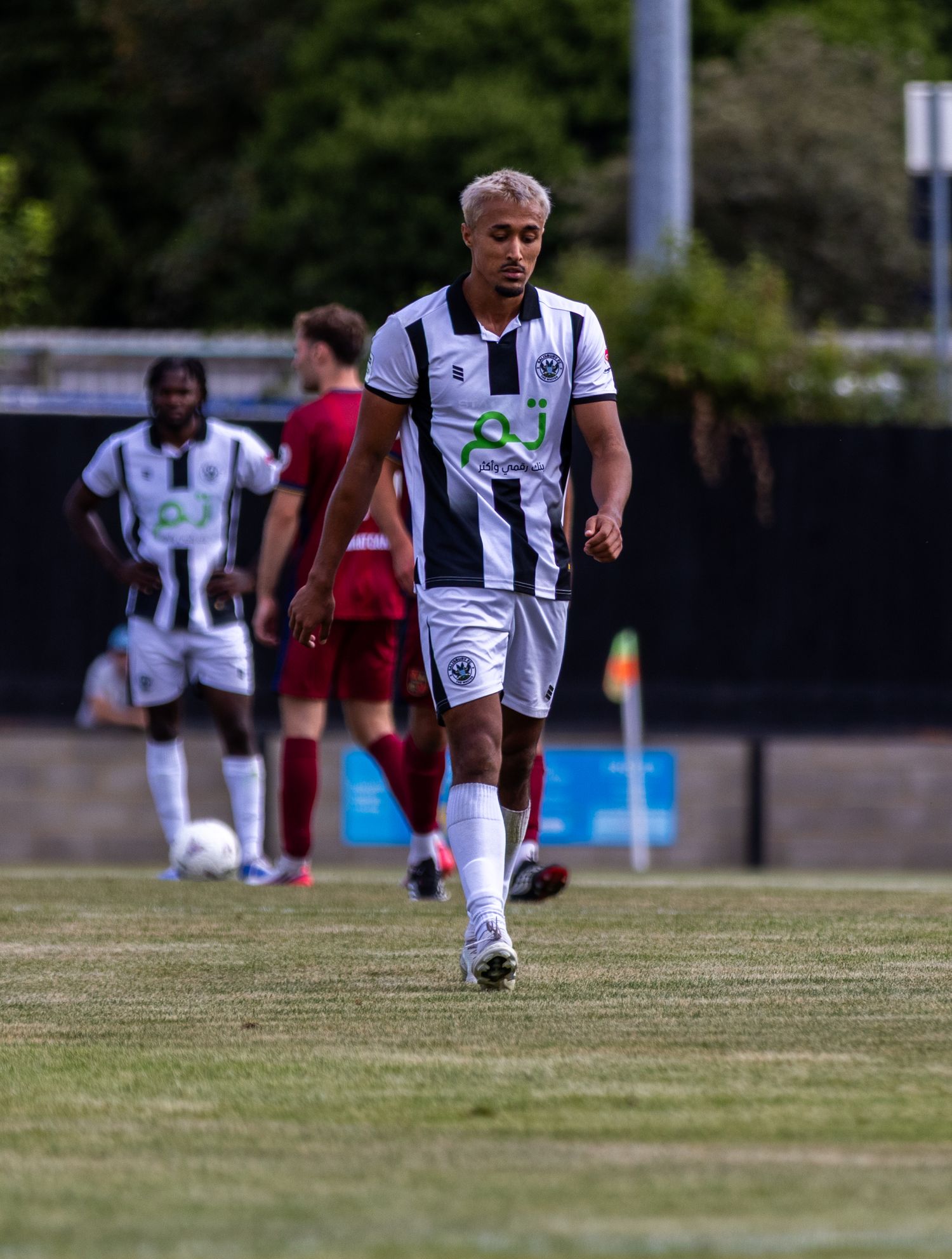A blonde footballer in black and white striped kit strides confidently across the pitch during a match.